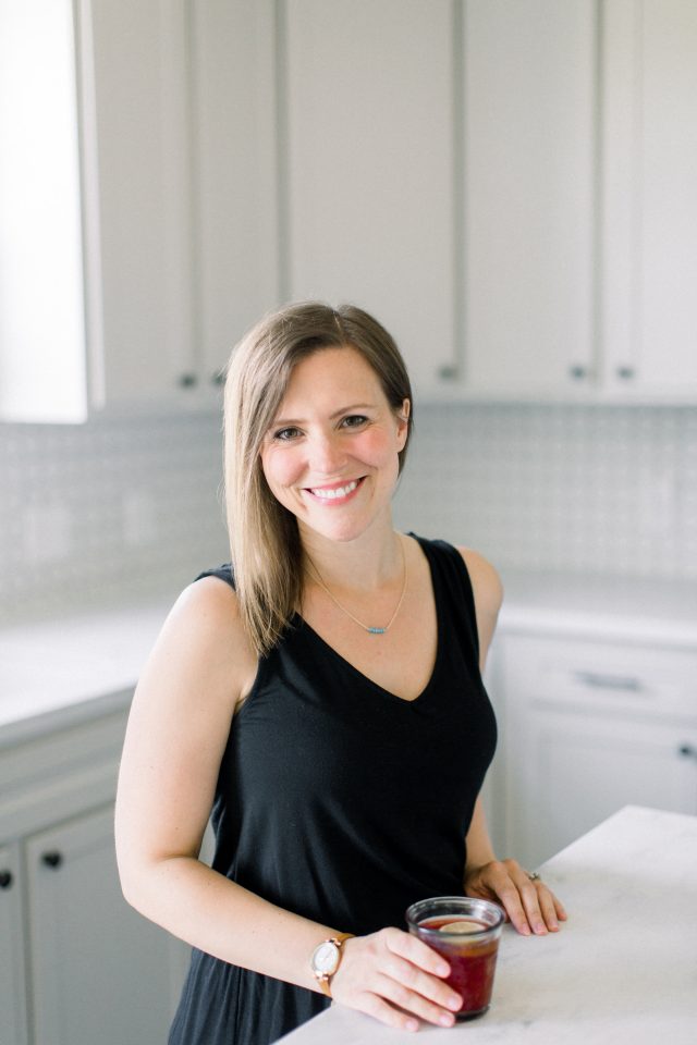 A white kitchen with CEO, Erin Jensen, standing at the kitchen island.