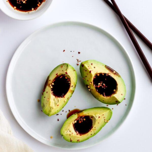 Three sections of avocado on a white plate filled with soy sauce and next to a small dish of soy sauce.