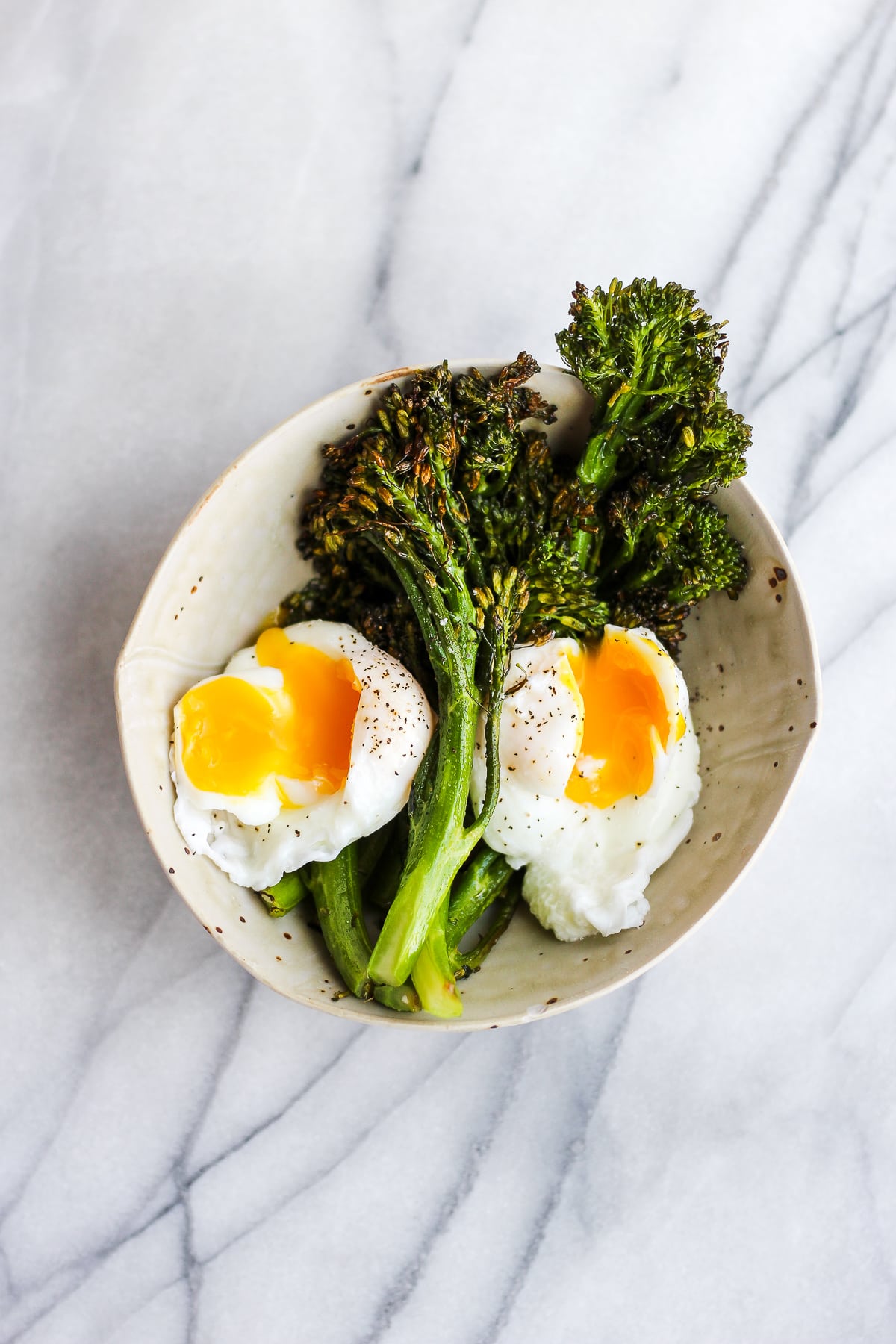 Roasted broccolini in a bowl with two poached eggs.
