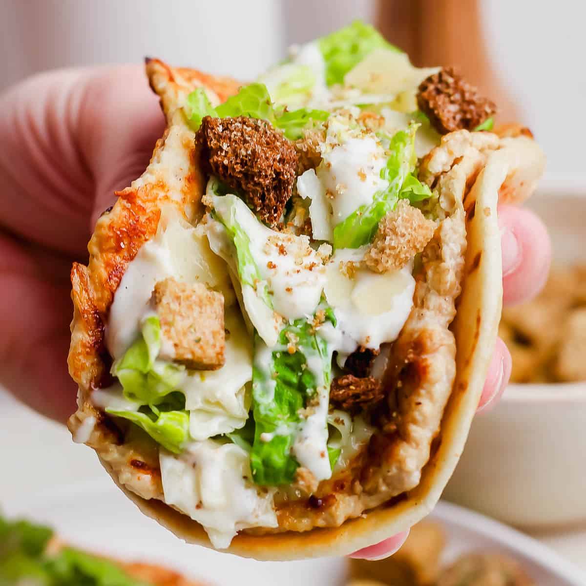 Someone holding a chicken caesar smash burger taco with crushed croutons on top.