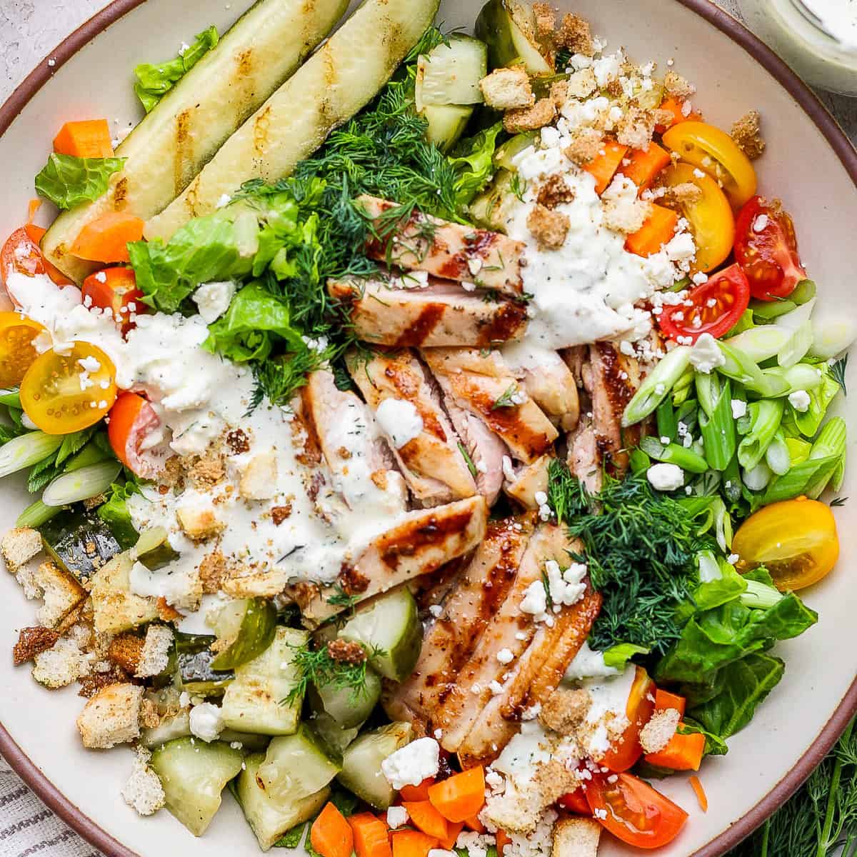 A big bowl of a dill pickle chicken chop salad with grilled pickles, chicken thighs, carrots and dill.