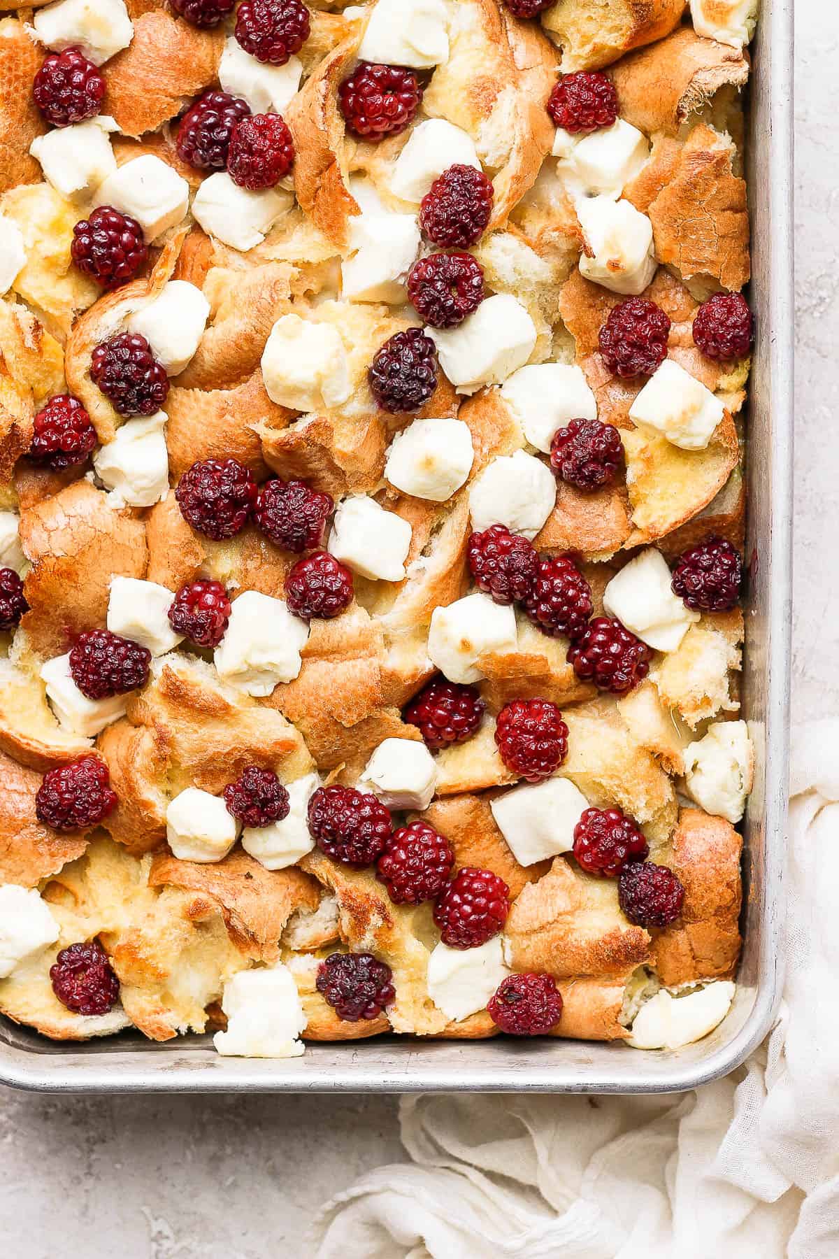 A baking dish with french toast bake inside with blackberries and cream cheese on top. 