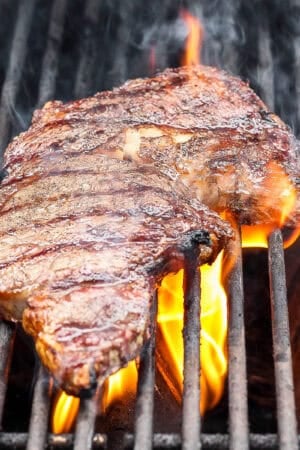 A ribeye steak on the grill with a flare up of fire.