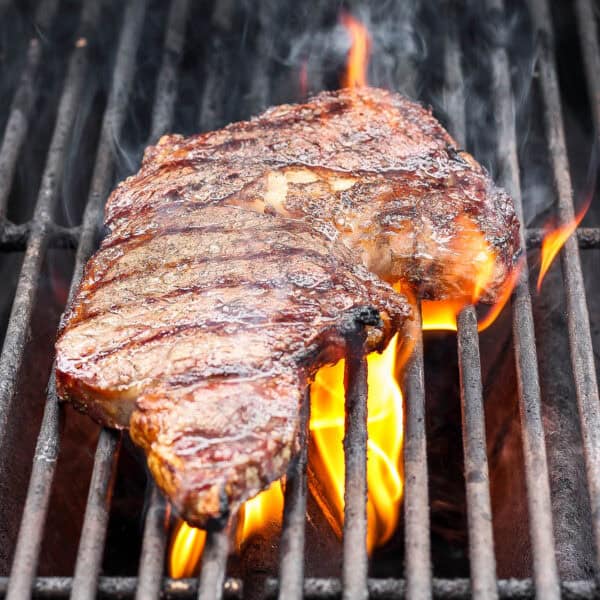 A ribeye steak on the grill with a flare up of fire.