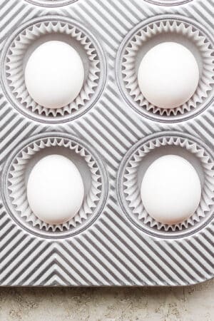 Six eggs sitting in muffin tins with muffin liners.