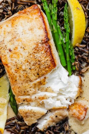 A plate of wild rice, asparagus, lemon wedges, lemon beurre blanc and pan seared halibut.