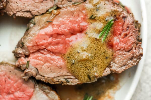 Slices of roasted beef tenderloin on a white plate with pan sauce and fresh rosemary.