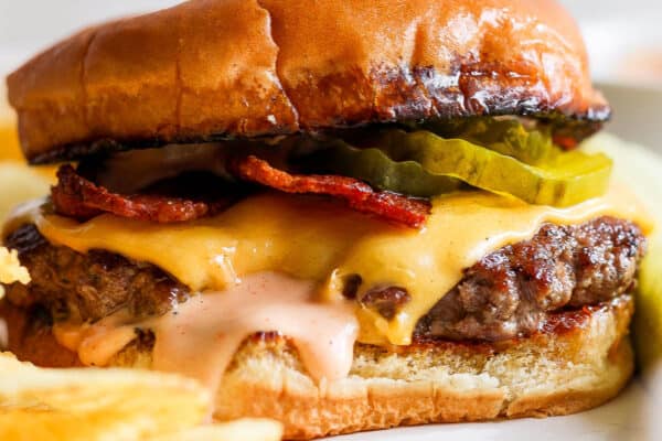 A smash burger on a plate with melted cheese, burger sauce, bacon and pickles on a toasted bun.