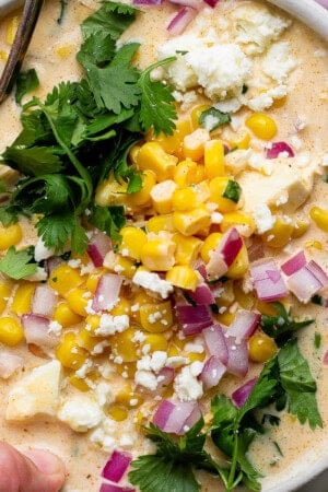 A bowl of mexican street corn white chicken chili with fresh cilantro, red onion and crumbled feta cheese on top.