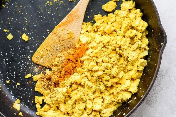 Cooked tofu scramble in a cast iron skillet with a wooden spoon sticking out.