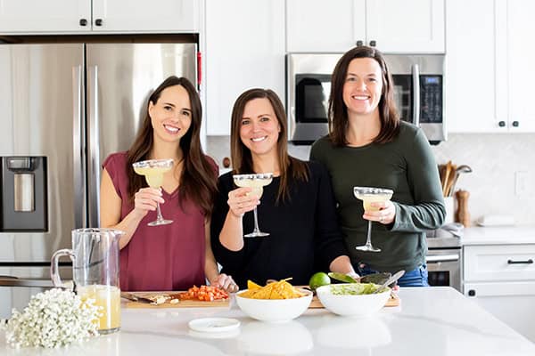 The three women on the Wooden Skillet team in a kitchen and each one is holding a margarita.