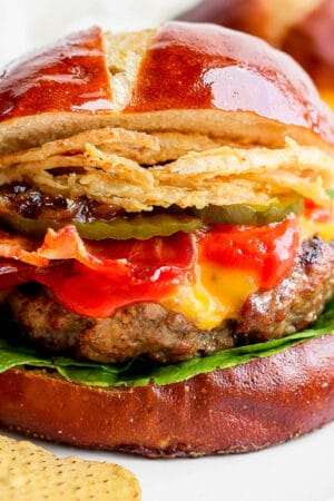 A grilled burger on a pretzel bun with lettuce, ketchup, bacon, pickles and fried onions.