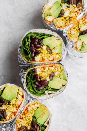 Three vegan breakfast burritos that were each wrapped in foil and cut in half to see the inside.