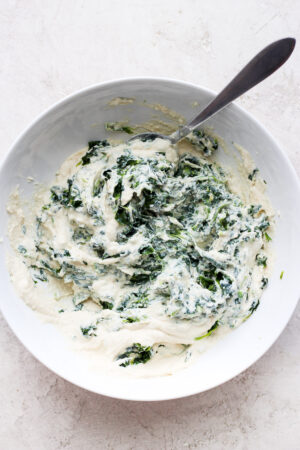 A white bowl with vegan ricotta fully mixed with a spoon.