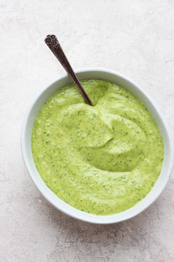 A bowl of creamy chimichurri sauce with a spoon sticking out the side.