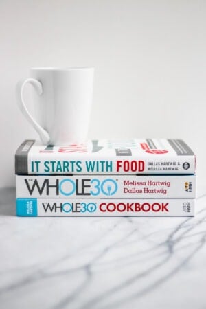 A stack of three Whole30 books with a white mug on top.