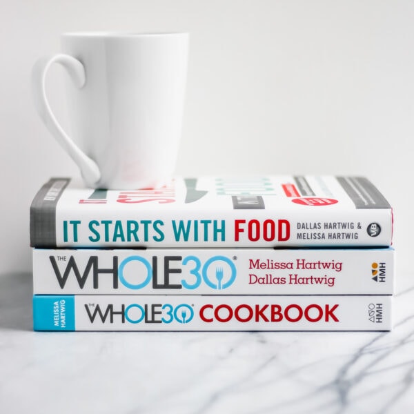 A stack of three Whole30 books with a white mug on top.